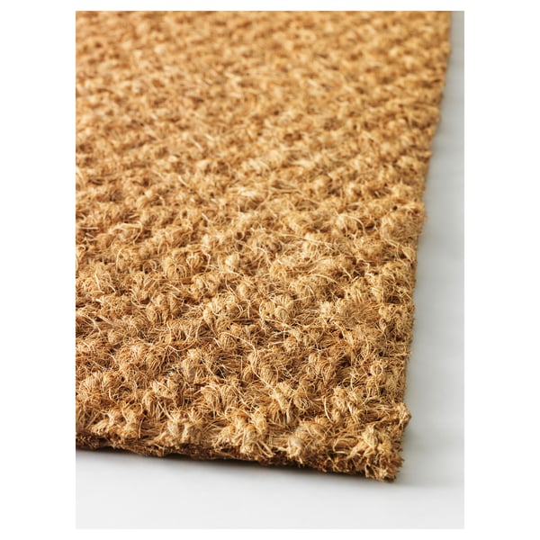 Capacho com superfície de fibra de coco texturizada, fibras naturais, espessas e duráveis. Exibido em fundo branco, vista angular.