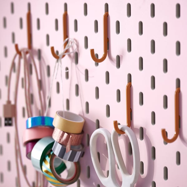 Pegboard com ganchos laranja segurando fitas coloridas e tesouras brancas, organizado para artesanato ou uso em escritório.