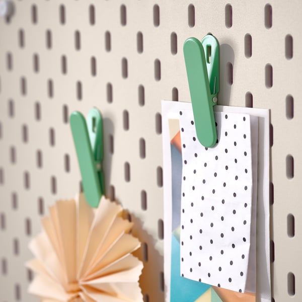 Pegboard montado na parede com prendedores de roupa verdes segurando itens de papel; um leque de papel abaixo deles.