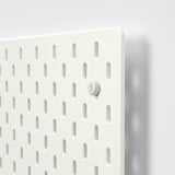 Pegboard branco com orifícios uniformemente espaçados, com um botão central branco, fixado a uma parede lisa.