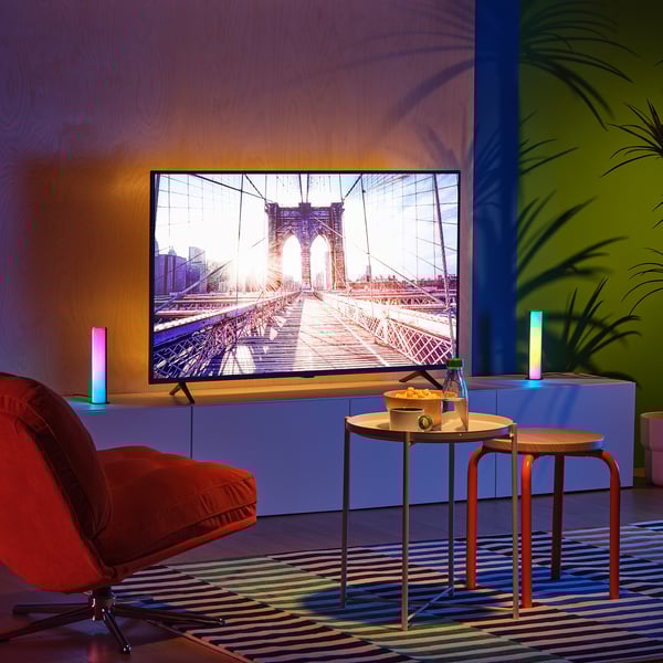 TV moderna na sala de estar colorida com ponte brooklyn na tela. Cadeira vermelha, mesas, tapete, plantas, luzes coloridas.