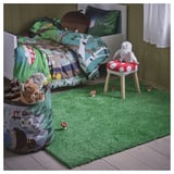 Quarto de criança com tapete verde SKOGSDUVA, materiais 100% reciclados. Tapete cobre o chão, cercado por brinquedos e cama. Superfície macia e fácil de brincar.