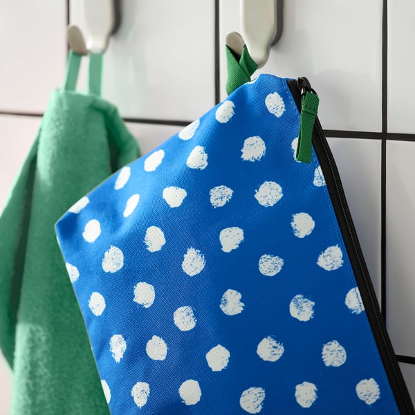 Bolsa de higiene azul com bolinhas brancas pendurada em um gancho, com zíper verde e compartimentos para organização.