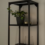 Prateleira de metal preto com luzes led; abriga plantas, vasos e velas.