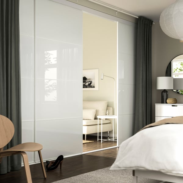 Quarto moderno com guarda-roupa grande, cama, vaso, janela, banquinho e cadeira.