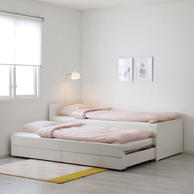 Cama individual SLÄKT branca brilhante com lençóis cor-de-rosa, candeeiro de leitura montado na parede, estruturas pequenas, tapete leve, design simples e minimalista, encaixa bem em divisões pequenas.