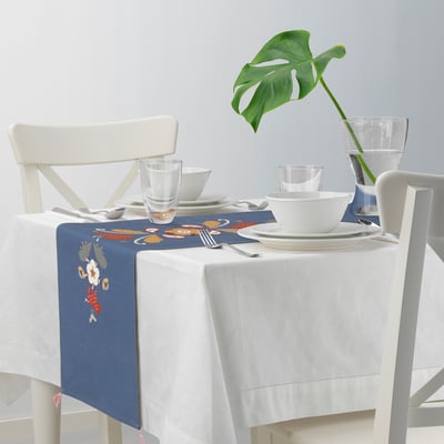 Caminho de mesa bordado azul em mesa coberta de branco, cercado por cadeiras brancas e copos transparentes.