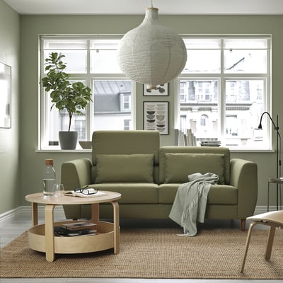 Sofá verde moderno em sala de estar aconchegante com janela grande, mesa de centro e luminária pendente.