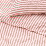 Close-up de lençol listrado rosa e branco, textura lisa e ondulada, cuidadosamente dobrada.