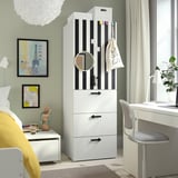 Quarto moderno com guarda-roupa SMÅSTAD, cartaz de Paris, cama aconchegante e escrivaninha com planta e fones de ouvido.