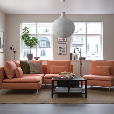 Sofá seccional laranja brilhante na sala de estar aconchegante com grande janela, luz pendente tecida, mesa de café preta, planta e arte.