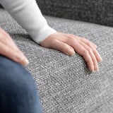 Pessoa sentada num sofá SÖRVALLEN cinzento, mãos apoiadas no apoio de braços. Design moderno e minimalista em tecido cinza escuro.