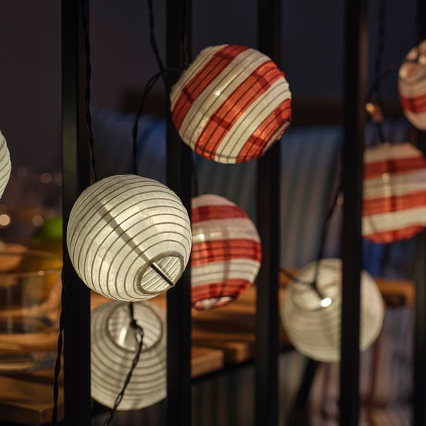 Cordão de luzes solares esféricas em vermelho, branco e translúcido, emitindo brilho suave, perfeito para espaços ao ar livre.