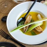 Prato fundo branco com legumes assados e molho, acompanhado de talheres pretos.