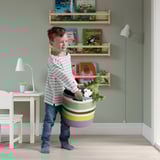 Menino carregando uma cesta de tecido colorido cheia de brinquedos de pelúcia, indicando o uso de STRANDSKATAs para armazenamento e portabilidade de brinquedos.