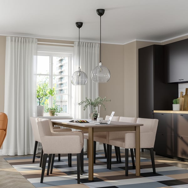 Conjunto de jantar moderno com mesa STRANDTORP, cadeiras bege, luminárias pendentes e janelas grandes.
