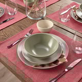 Conjunto de mesa com tigelas verdes, talheres, guardanapos vermelhos, copos em jogos americanos vermelhos.