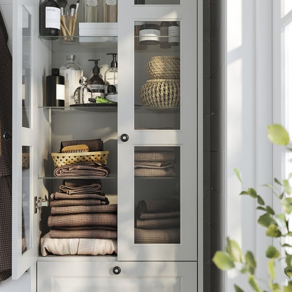 Armário de banheiro com portas de vidro com prateleiras e gavetas para guardar toalhas e produtos de higiene pessoal.