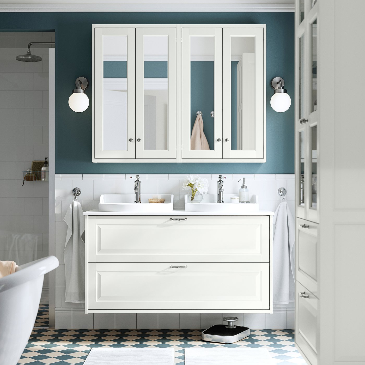 Banheiro branco moderno com grande penteadeira, pia e armário com espelho. O piso tem azulejos azul-acinzentados. Toalhas montadas, luminárias e acessórios.