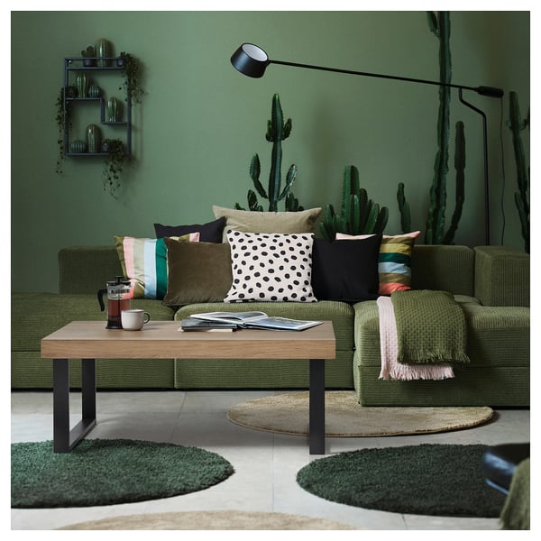 Sala de estar verde moderna com mesa de centro TARSELE, vegetação, almofadas coloridas e luminária de chão.