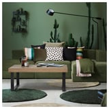 Sala de estar verde moderna com mesa de centro TARSELE, vegetação, almofadas coloridas e luminária de chão.