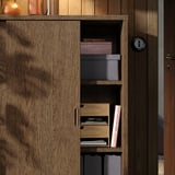 Guarda-roupa com estantes abertas exibindo caixas e livros, ao lado de uma porta de madeira fechada. Mostra prateleiras ajustáveis para armazenamento personalizável.