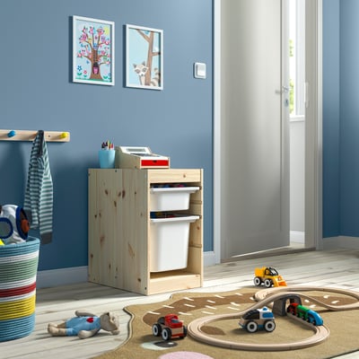 Módulo de arrumação TROFAST com caixotes brancos, contendo brinquedos e materiais de arte, ao lado da parede azul.