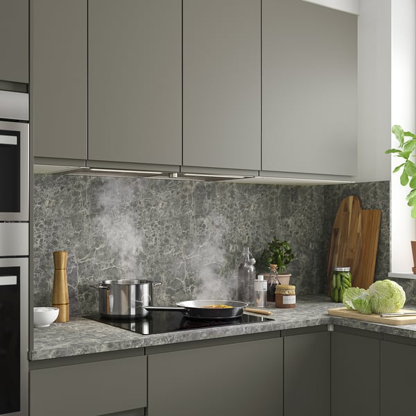 Cozinha moderna com armários cinza, cooktop preto, exaustor de aço inoxidável, backsplash de mármore e utensílios de bancada e vegetação.