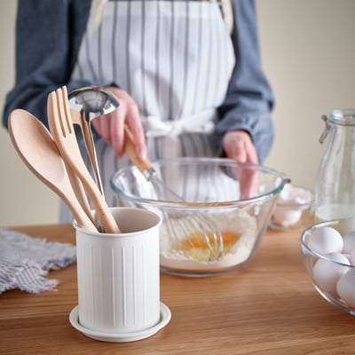 Pessoa cozinhando com utensílios de madeira e tigela de vidro.