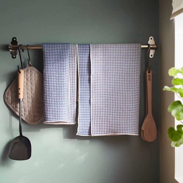 Rack de parede com toalhas de cozinha penduradas, luva de forno e utensílios de madeira.