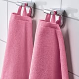 Duas toalhas felpudas rosa penduradas perfeitamente em ganchos montados na parede, exibindo sua textura absorvente e macia e tecido de costela de secagem rápida.