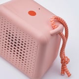 Alto-falante pequeno e portátil com um design durável e à prova d'água. Rosa brilhante com superfície texturizada e cabo de corda laranja trançado.