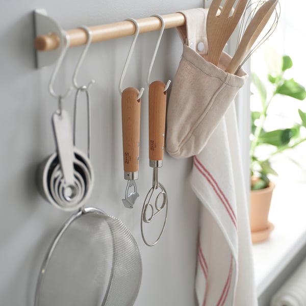 Um organizador de cozinha com ferramentas penduradas, incluindo um batedor de massa dinamarquês e copos medidores, armazenados de forma eficiente para fácil acesso.