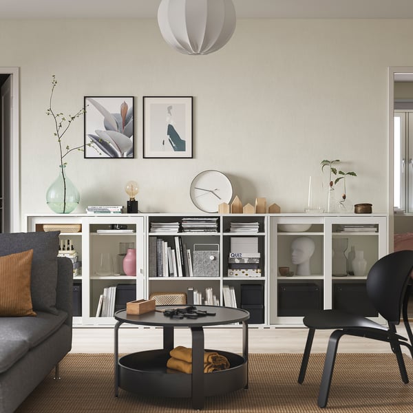 Sala minimalista com arrumação cinzenta, portas de vidro, livros, vasos, decoração. tapeçarias, luz pendente, sofá cinza, cadeira preta, mesa de café, tapete.