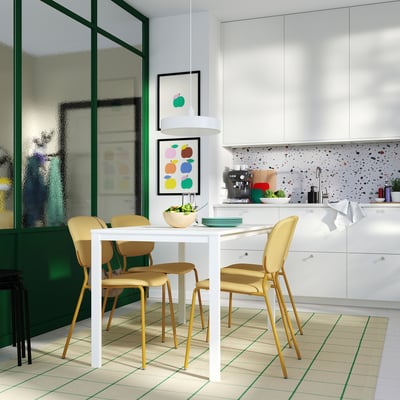 Cozinha moderna com mesa branca, quatro cadeiras amarelas, assentos acolchoados com espuma e parede de vidro com moldura verde.