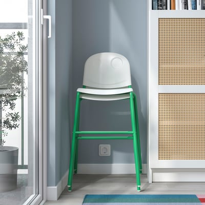 Uma cadeira júnior branca e verde colocada em uma sala, ideal para as crianças se sentarem à mesa, com empilhável e antiderrapante.