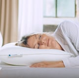 Uma mulher dorme pacificamente em um travesseiro VILDKORN, branco com bordas macias e de apoio, coberto por um cobertor branco.