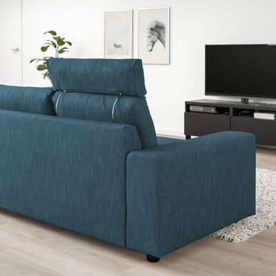 Um sofá VIMLE azul com encostos de cabeça numa sala de estar. É grande, combinando com uma TV montada na parede e um tapete. O design é moderno com almofadas de pelúcia.