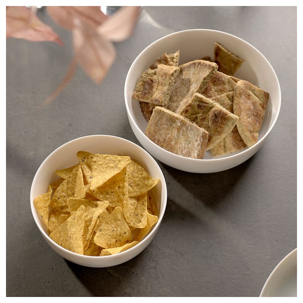 Duas tigelas de cerâmica branca, uma cheia de lascas triangulares amarelas, a outra com torradas retangulares marrons, colocadas em uma mesa cinza.