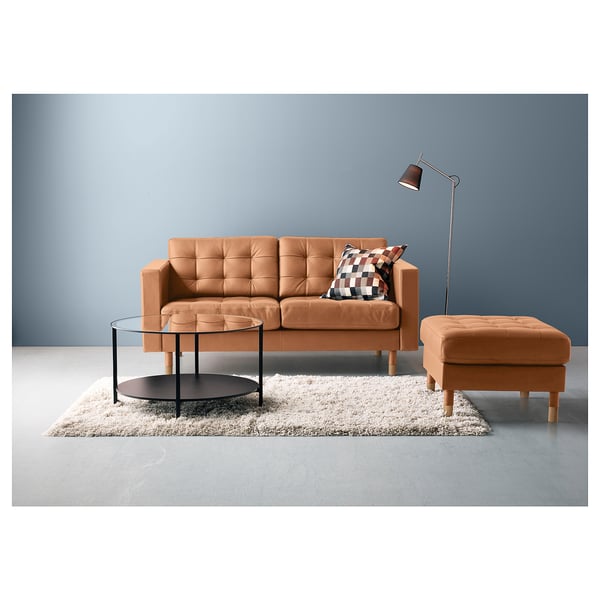 Configuração moderna da sala de estar com sofá laranja, apoio para os pés combinando, mesa de centro de vidro e luminária de chão contra a parede azul.