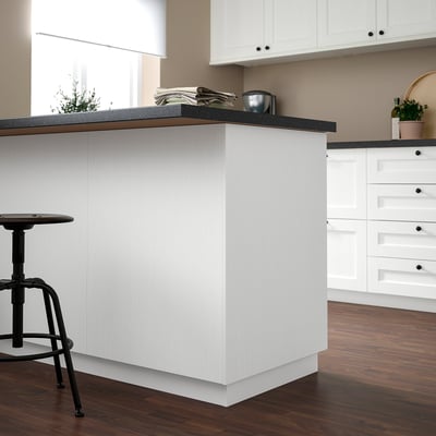 Modern white kitchen island with black countertop, stool, magazines, and plant. Cabinets extend above.
