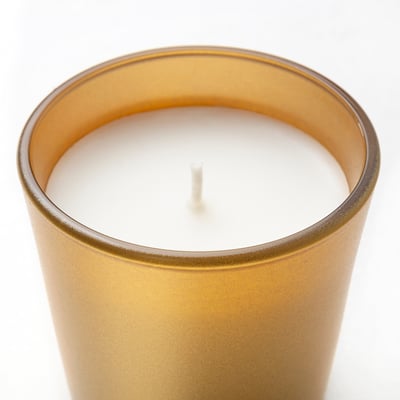 Golden cylindrical candle jar with white wax and cotton wick, sits alone against white.