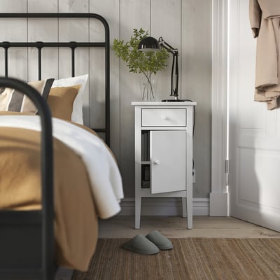 Bedroom with white GULLABERG bedside table, black lamp, green slippers, and bed with gold and white linens.