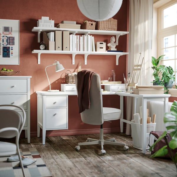 White l-shaped GULLABERG desk in corner with shelves, chair, and lamp.