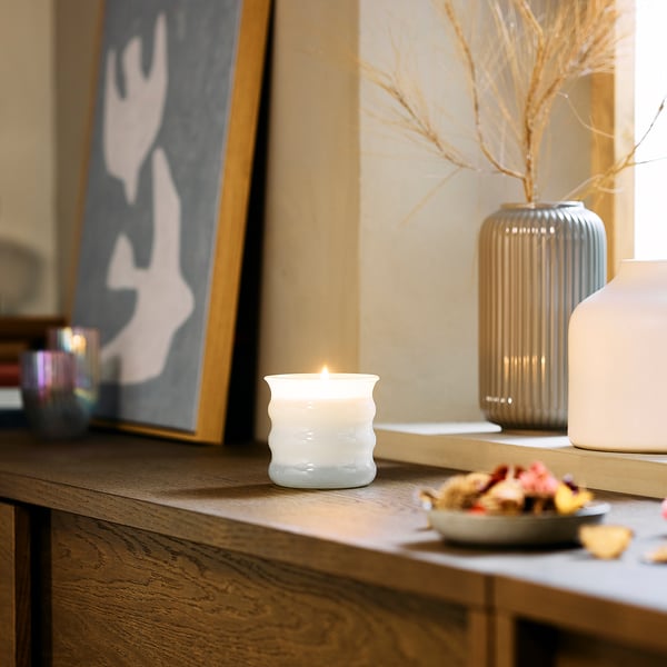 JUVELTRAST candle on wooden shelf with vases, creating cosy atmosphere.