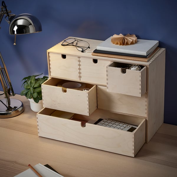 A wooden storage unit with multiple drawers, storing various items like a calculator, stationary, and accessories.