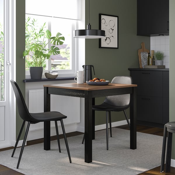 Small, modern black dining set with wooden table, two upholstered chairs, green walls.