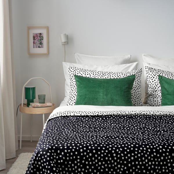 Dormitor modern cu lenjerie de pat alb-negru ÅSVEIG, perne din catifea verde, măsuță laterală rotundă albă cu decor verde și artă de perete colorată.