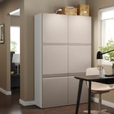 Unitatea de depozitare gri mare BESTÅ cu două uși se află lângă masa de luat masa, cu un design elegant și modern pentru organizarea casei.