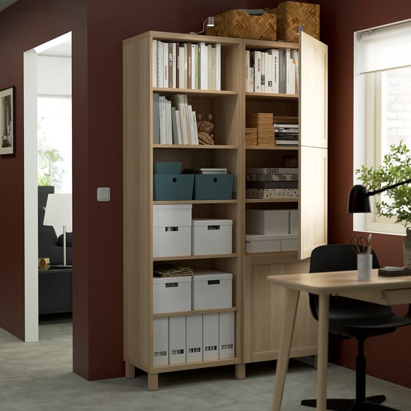 O bibliotecă din lemn BESTÅ depozitează diverse cutii de depozitare, cărți și articole. Rafturile sunt reglabile, prezentând versatilitatea organizațională.